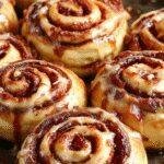 A plate of Maple Bacon Cinnamon Rolls with swirls of cinnamon filling, topped with icing and crispy bacon pieces, on a rustic wooden table.