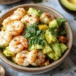 Colorful shrimp and avocado bowls topped with fresh mango salsa, garnished with herbs on a bright summer plate.
