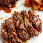 A beautifully plated beef brisket meal featuring tender, juicy slices of beef with a rich glaze, garnished with fresh herbs on a rustic wooden table, accompanied by side vegetables with a smoky, savory appearance.